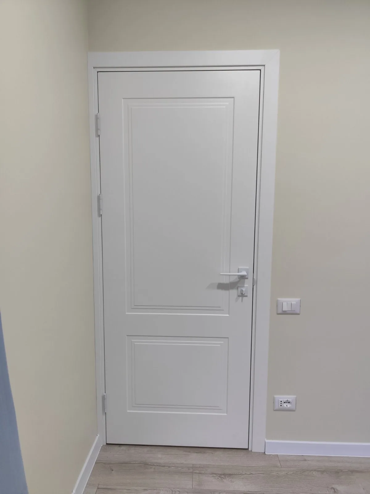 Ușă albă clasică, cu două panouri și mâner argintiu, pe un perete crem
