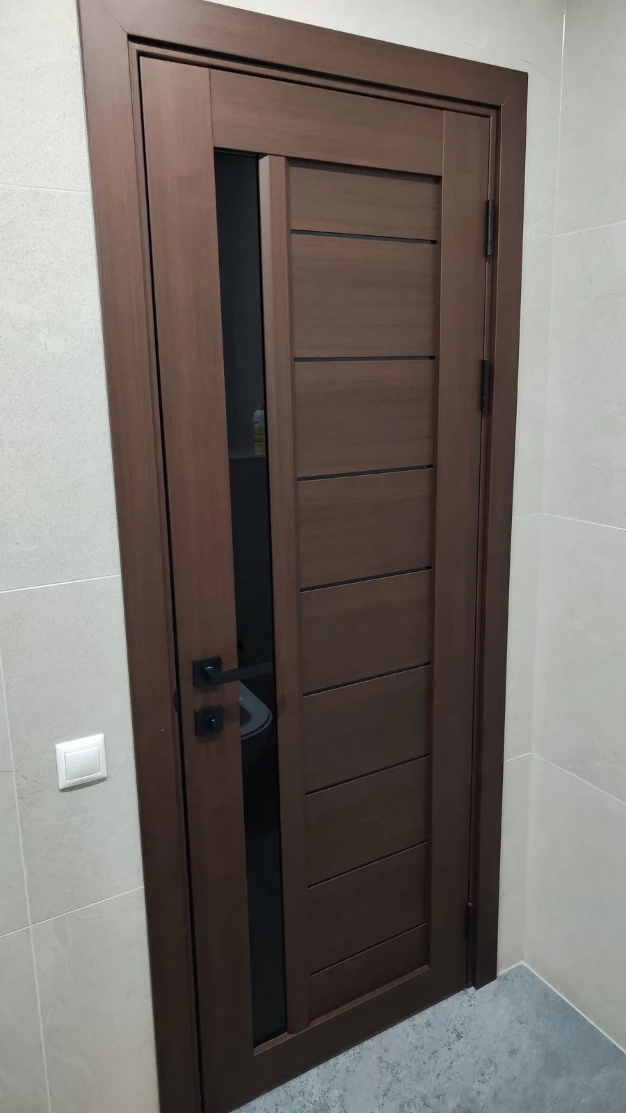 Ușă Bordo stejar închis, cu sticlă neagră și mâner negru, între pereți cu faianță deschisă
