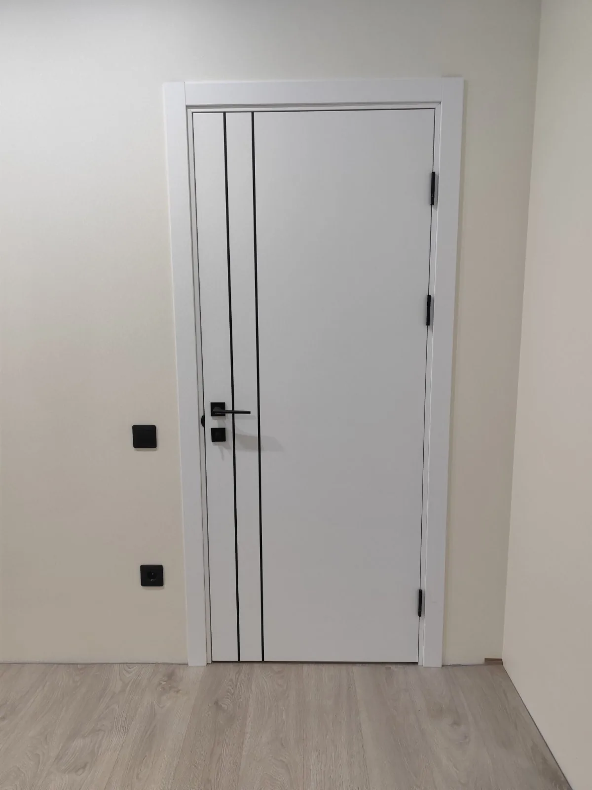 Ușă OD-01 albă emailată, cu două linii negre verticale și mâner negru, pe un perete crem