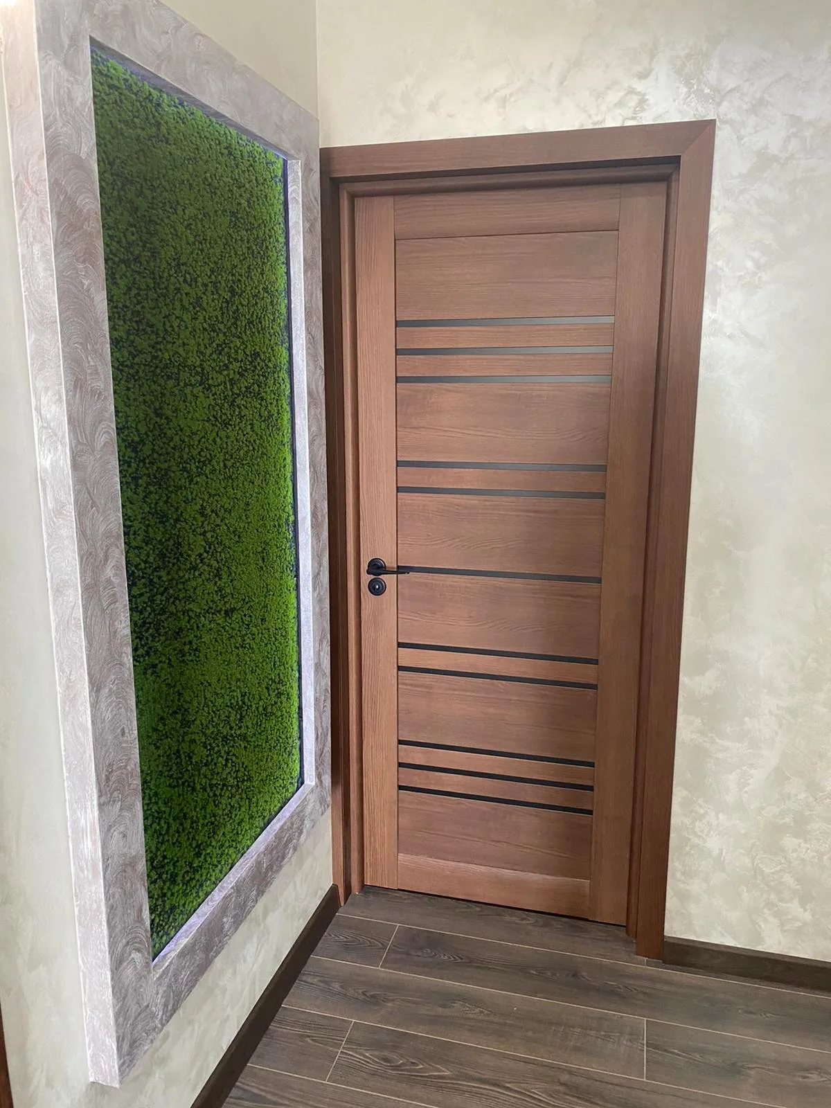 Ușă Versal în culoarea nuc regal, cu dungi de sticlă neagră, lângă un panou de mușchi verde